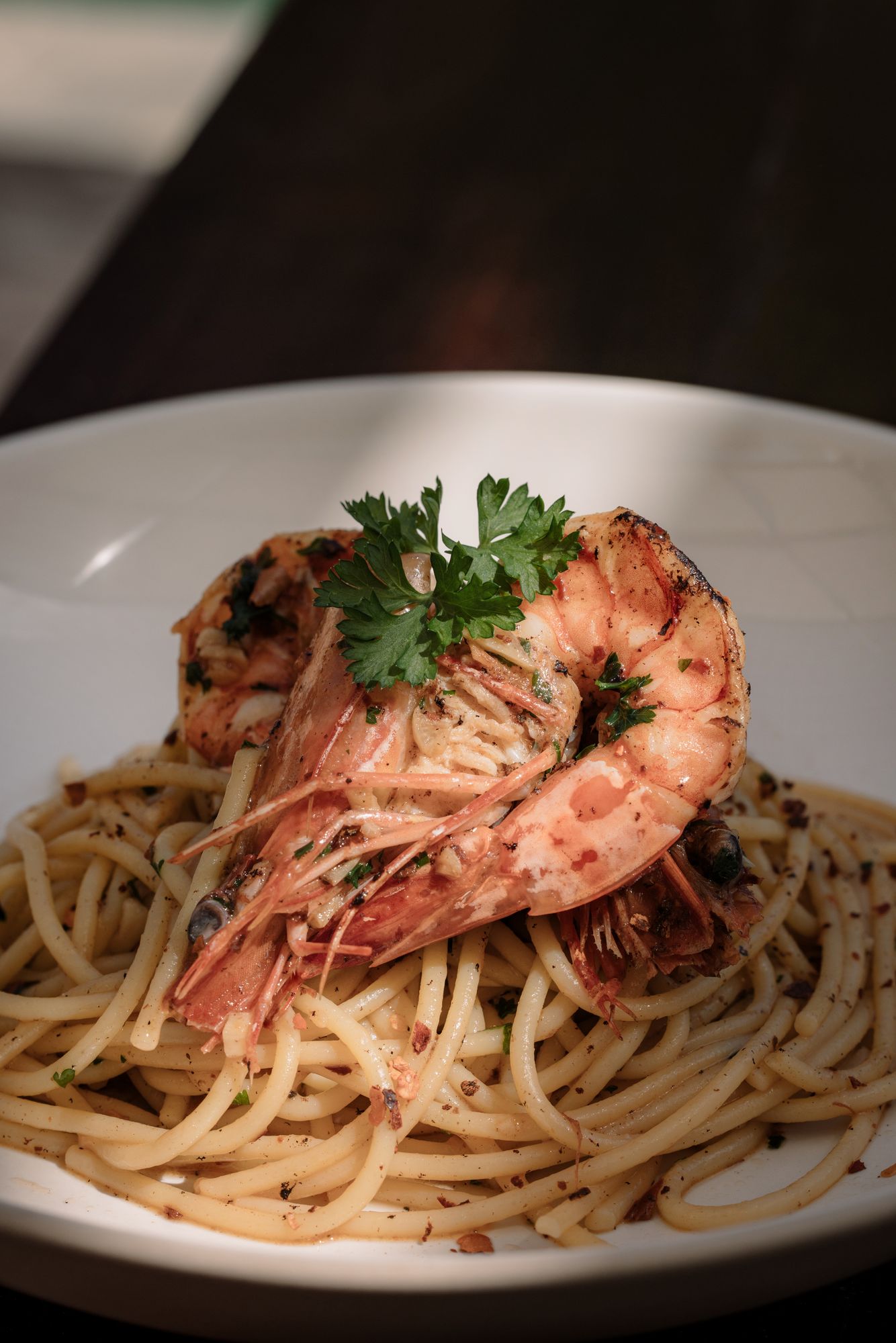 Spaghetti aglio e olio crowned with grilled king prawns and parsley in a wide white bowl.
