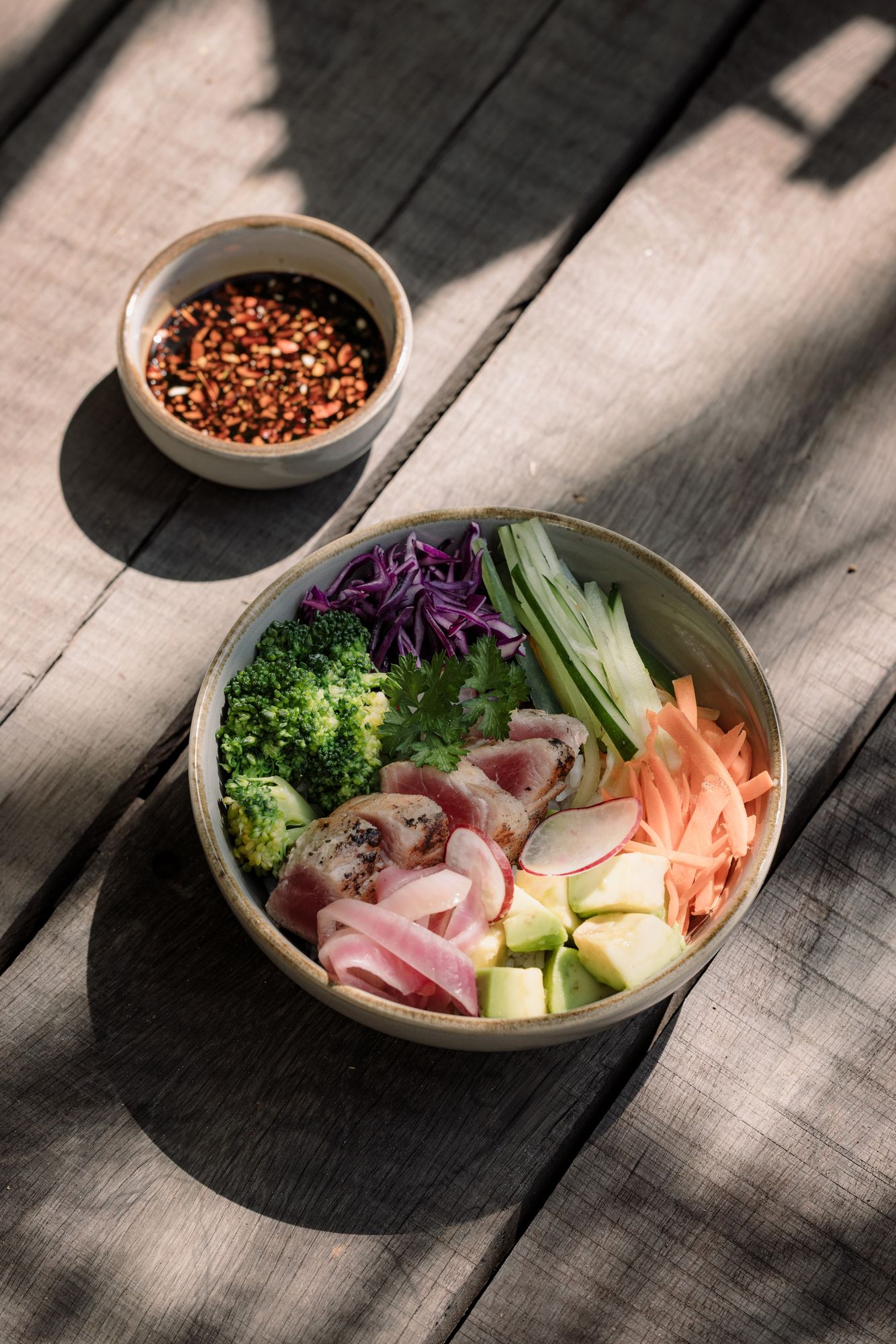 Bonnie’s bowl from above on a weathered wooden table: red cabbage, broccoli, cucumber, avocado, radish and carrot, with chilli on the side.