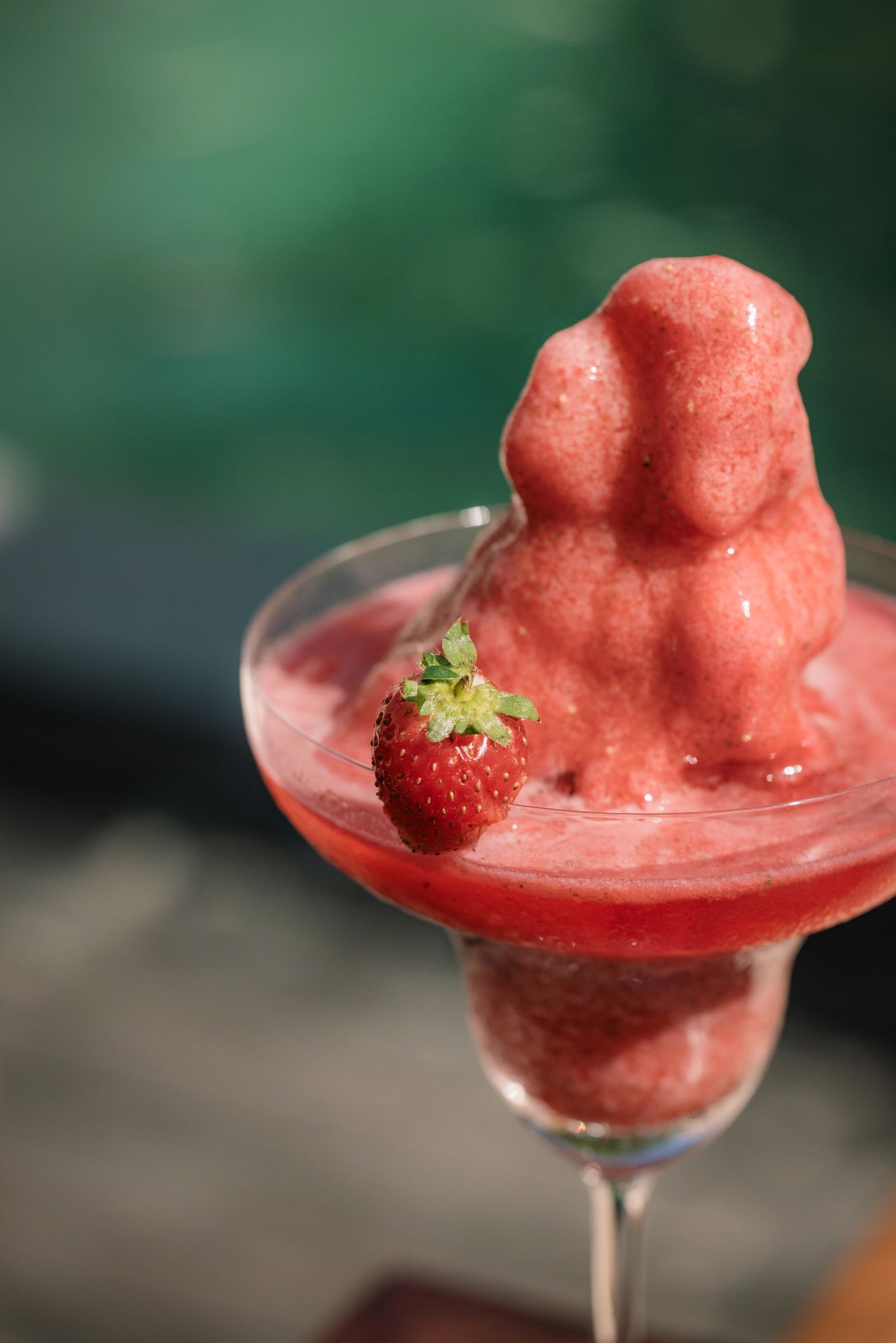 A frozen strawberry granita piled high in a coupe, a strawberry on the rim, the pool behind.