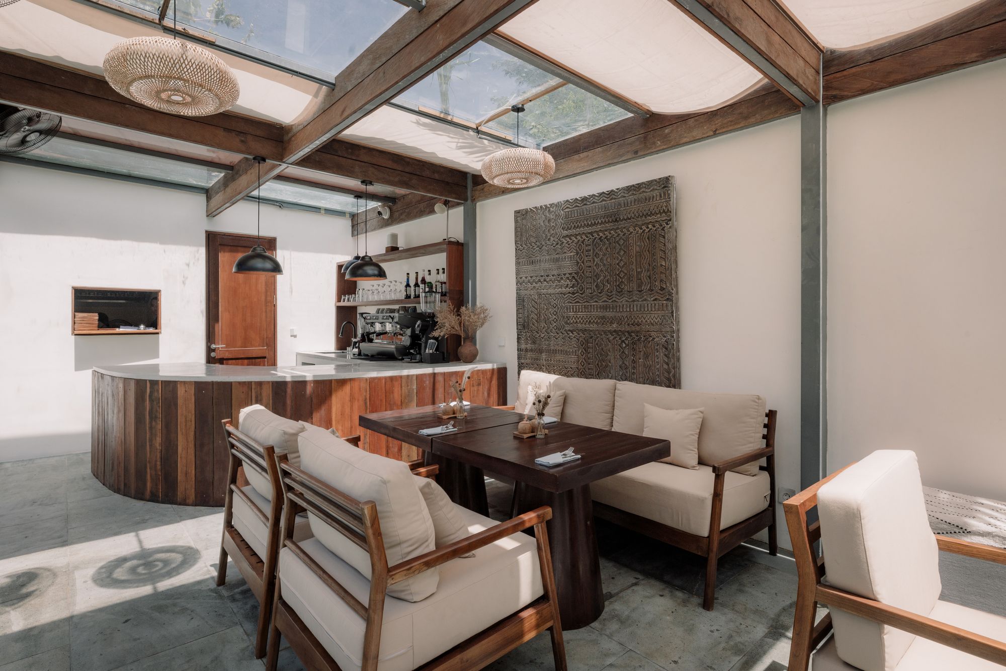 The lounge under the canvas roof in daylight, linen sofas around teak tables and the bar beyond.