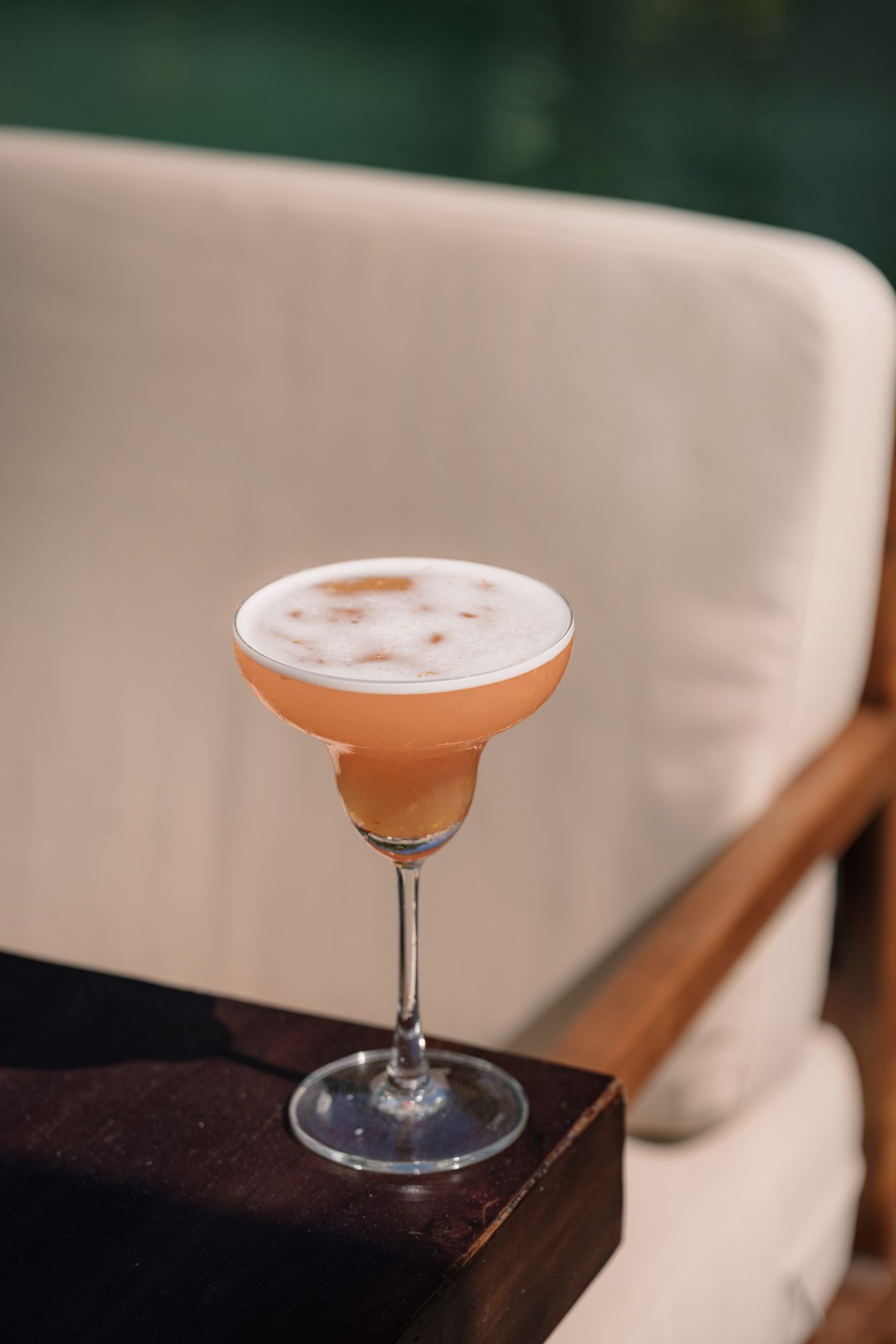 A Suasana Senja in a coupe, coral with a soft foam top, on a teak table by the pool.